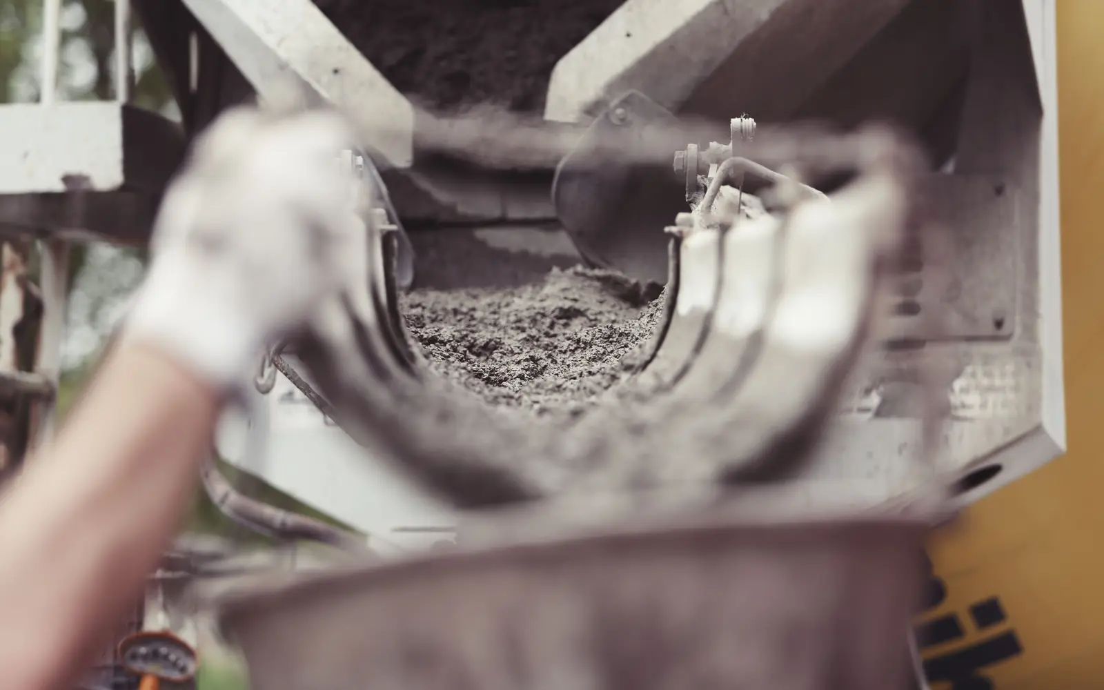 Concrete running down a mixer truck chute during a pour, a gloved hand guiding it