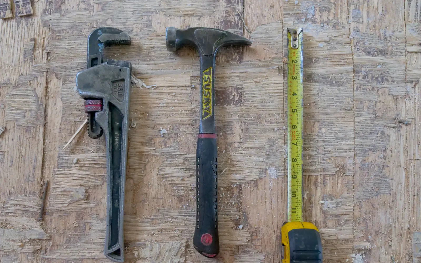 A hammer, wrench and tape measure laid out on a timber workbench